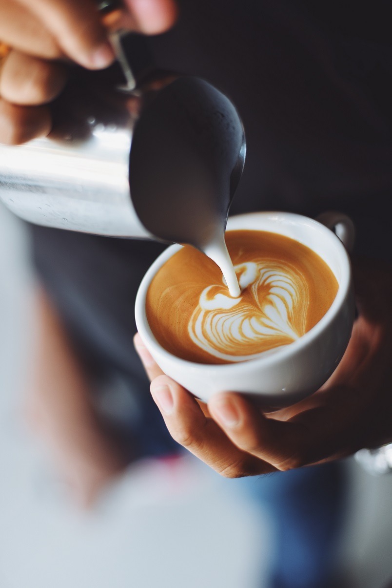 Una mano sosteniendo una taza de cafe cuando vierte leche sobre ella creando arte latte.