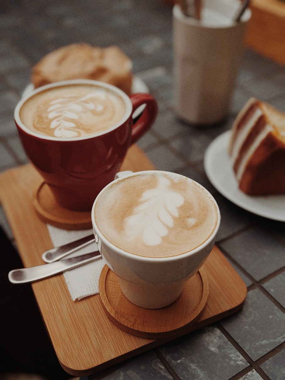 Dos tazas de cafe con arte latte color blanca y roja. Porción de budin.